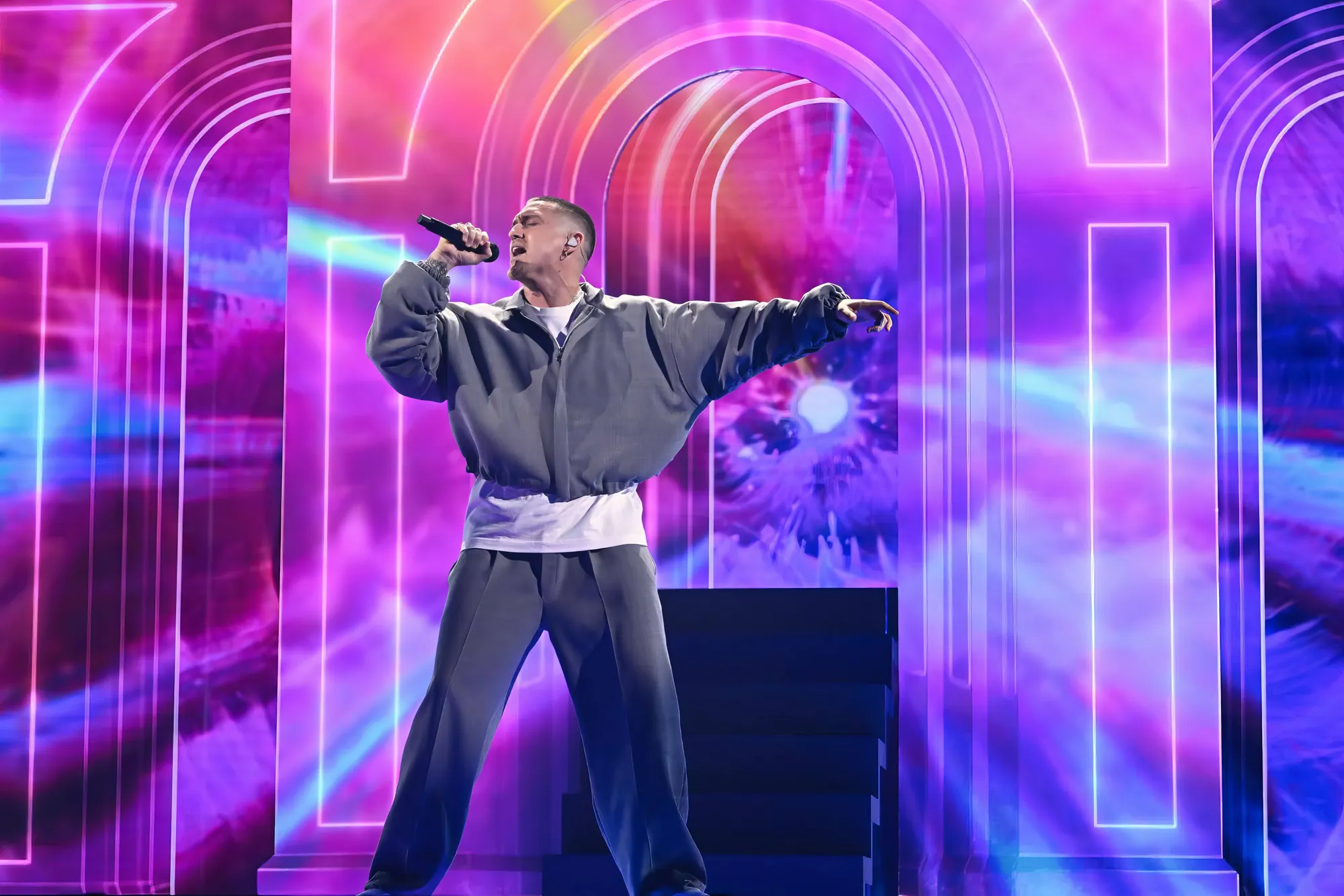 Danny Saucedo mid-performance, arms wide, against concentric pink and violet neon arches on the LED walls