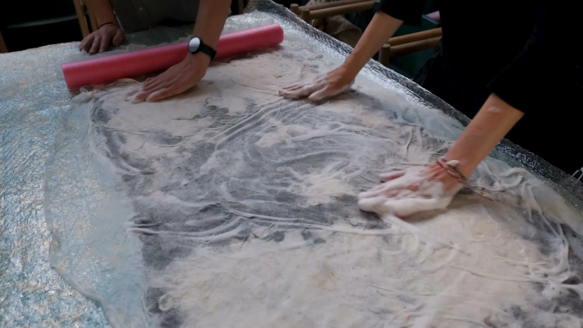 Hands felting the wool across the table